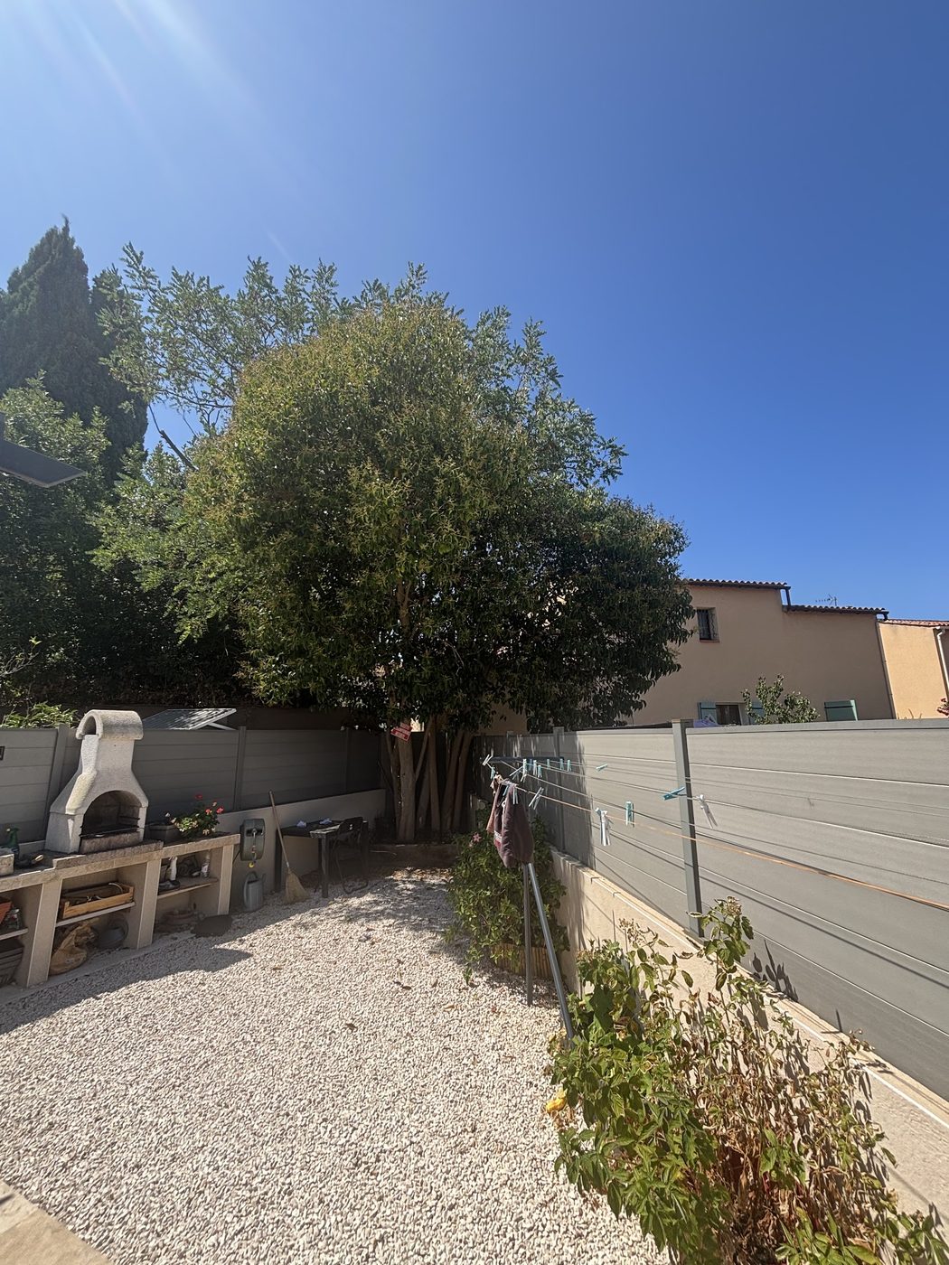 Jardin avec gravier blanc, arbre taillé et barbecue en pierre
