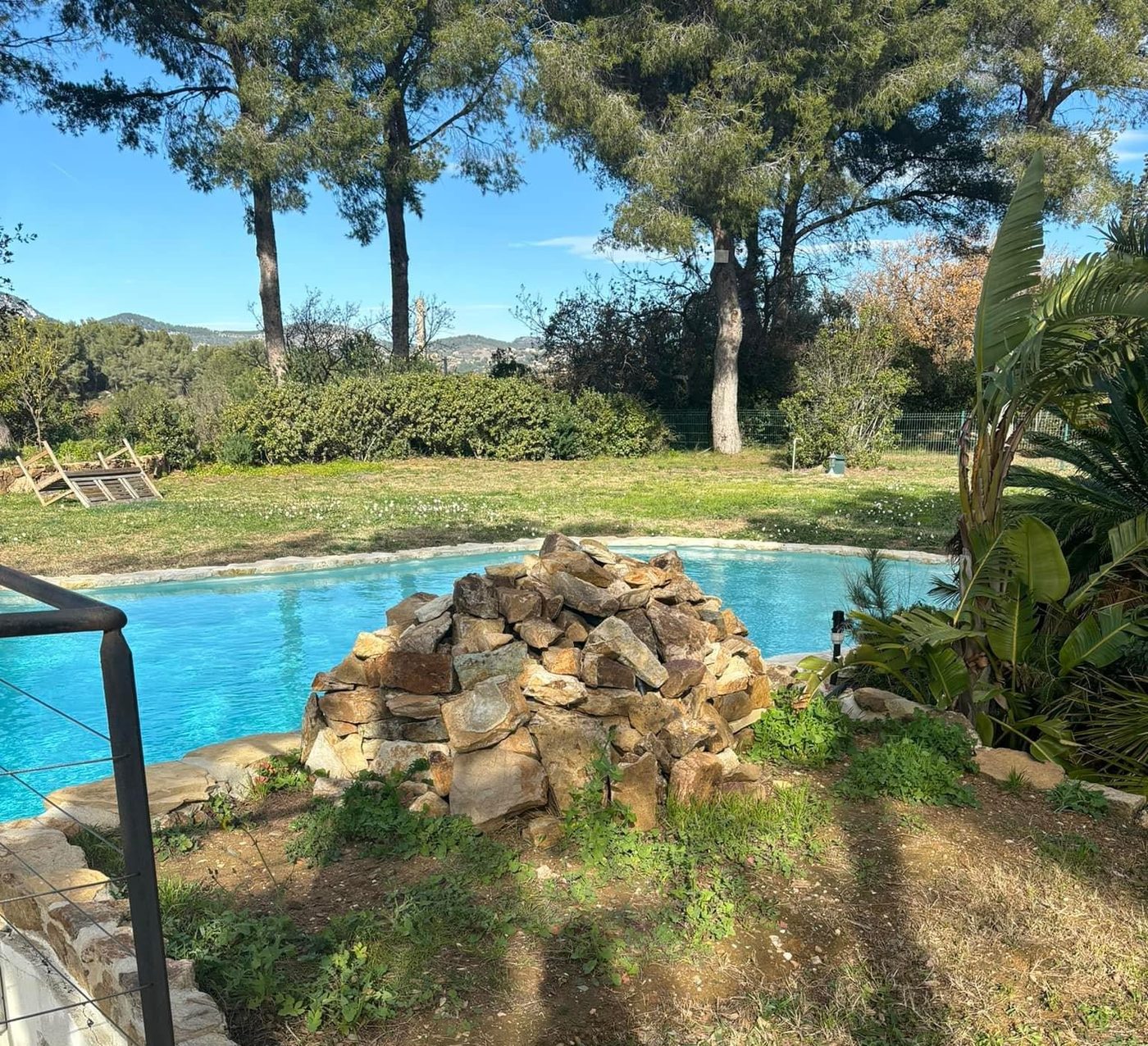 Abords de piscine avec rocaille et pelouse sous les pins
